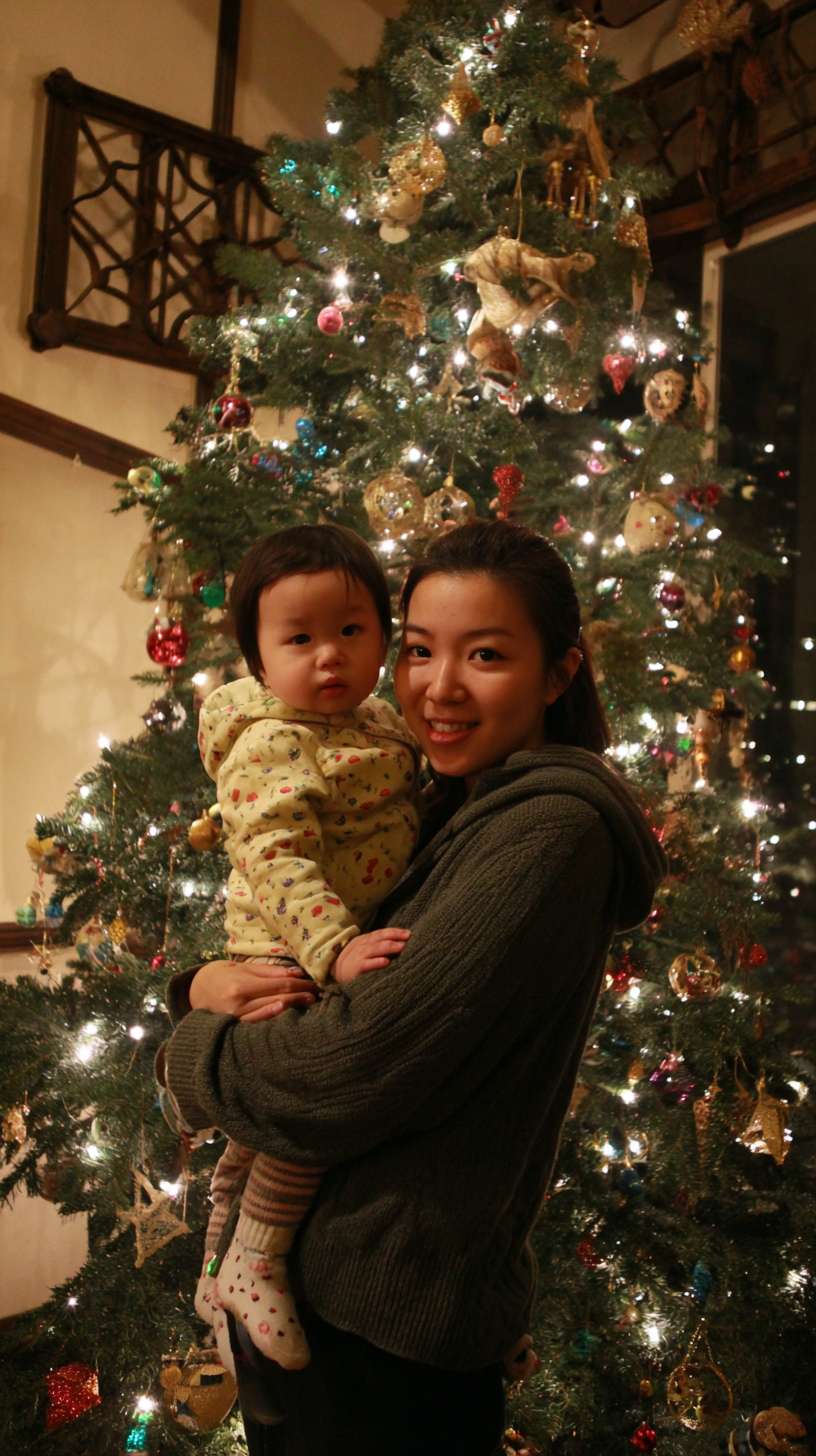 2圣诞树顶挂星星，妈妈托举孩子，树身缠绕彩灯，地面有未挂的袜子装饰，镜头从下往上推，温馨写实风 --ar 9:16 --v 7 --stylize 100 --fast --no 水印