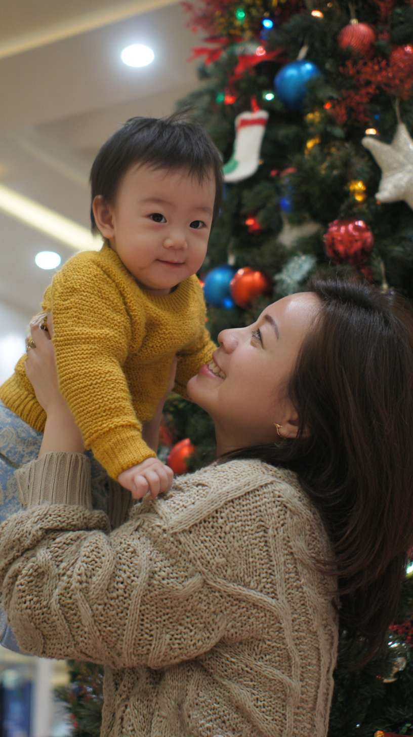 2圣诞树顶挂星星，妈妈托举孩子，树身缠绕彩灯，地面有未挂的袜子装饰，镜头从下往上推，温馨写实风妈妈孩子都金发 --ar 9:16 --v 7 --stylize 100 --fast --no 水印