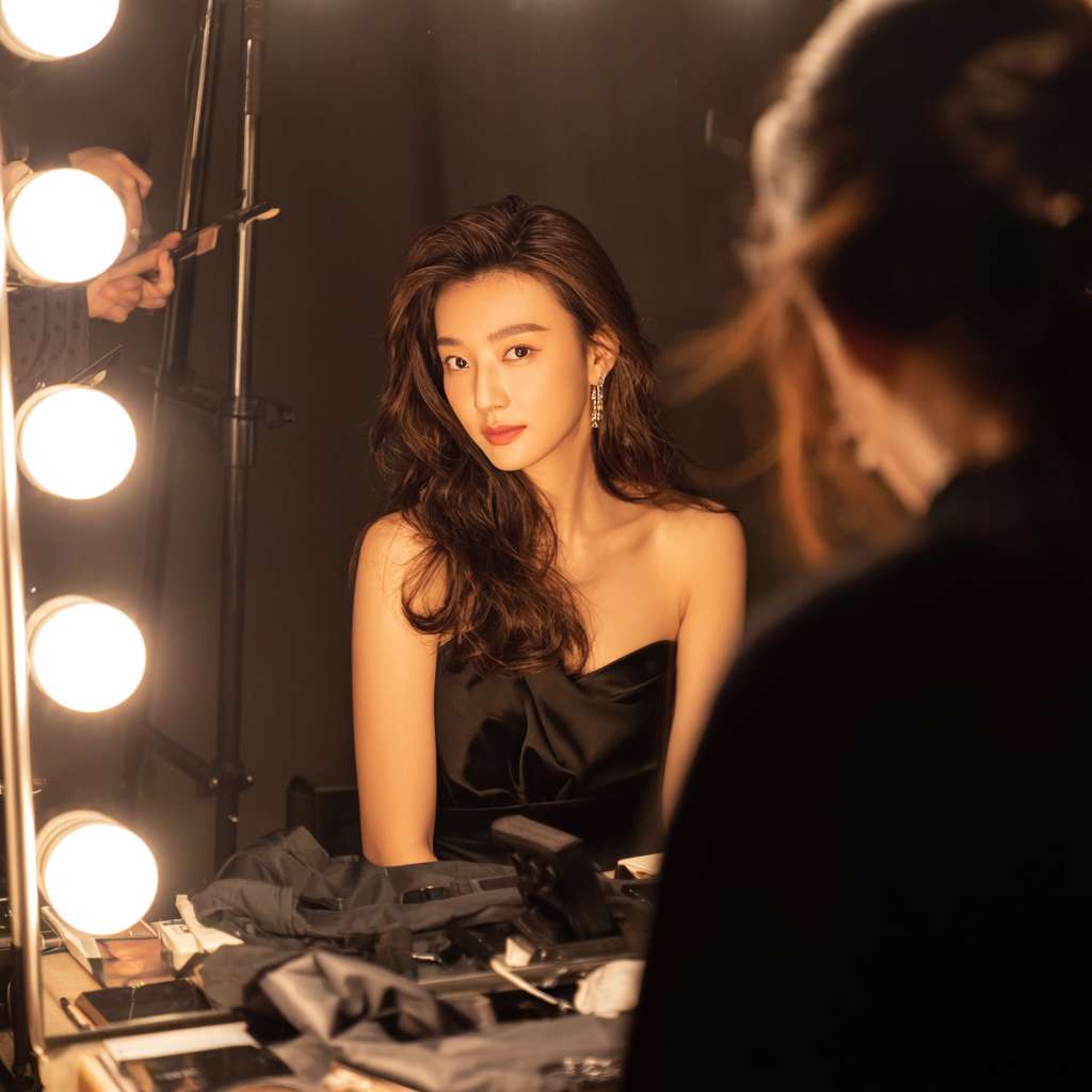女演员在后台做头发造型，有化妆师在帮她补粉，她看着一面专业的灯光化妆镜，还有造型师帮她在弄头发，画面是一个暖色调，女演员背对着镜子，镜子反射出她的容貌 --ar 1:1 --v 7 --stylize 100 --fast --no 水印
