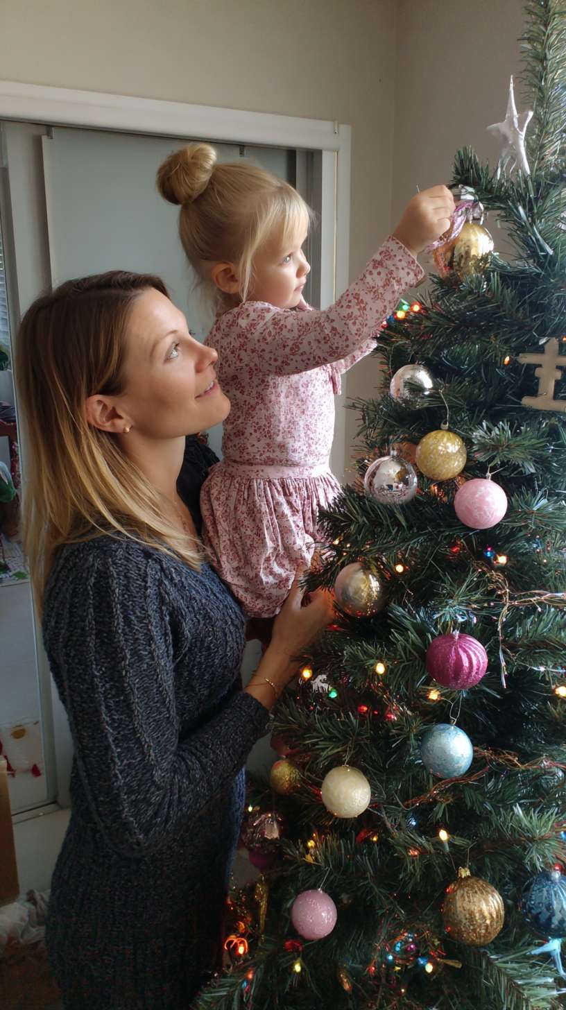 2圣诞树顶挂星星，妈妈托举孩子，树身缠绕彩灯，地面有未挂的袜子装饰，镜头从下往上推，温馨写实风妈妈和孩子都金发，妈妈轧丸子头 --ar 9:16 --v 7 --stylize 100 --fast --no 水印