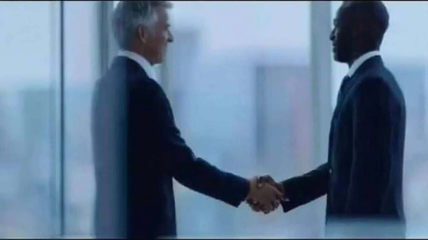 两个中年男人，亚洲人种，深色皮肤，短发，穿着深色西装，正在一个现代办公室环境中握手，背景是大面积的玻璃窗，透过玻璃可以看到外面的城市景观，光线明亮，整体氛围正式而专业。男人们在画面的中心位置，握手的手部占据画面的大部分，背景的玻璃窗和城市景观模糊处理，突出前景的握手动作。画面风格为照片现实主义，整体色调偏冷，突显专业和正式的场合。 --ar 16:9 --v 7 --stylize 100 --fast --sref https://img-xpc-mj0.xpccdn.com/prod/upload/34fe3e9c-221a-4842-b265-184af228609c/09f5db4c04c225adf9fea1c6bf839cad.png~tplv-5yakomv5zn-auto-v1%3A1024%3A0%3Aq75.jpg --no 水印