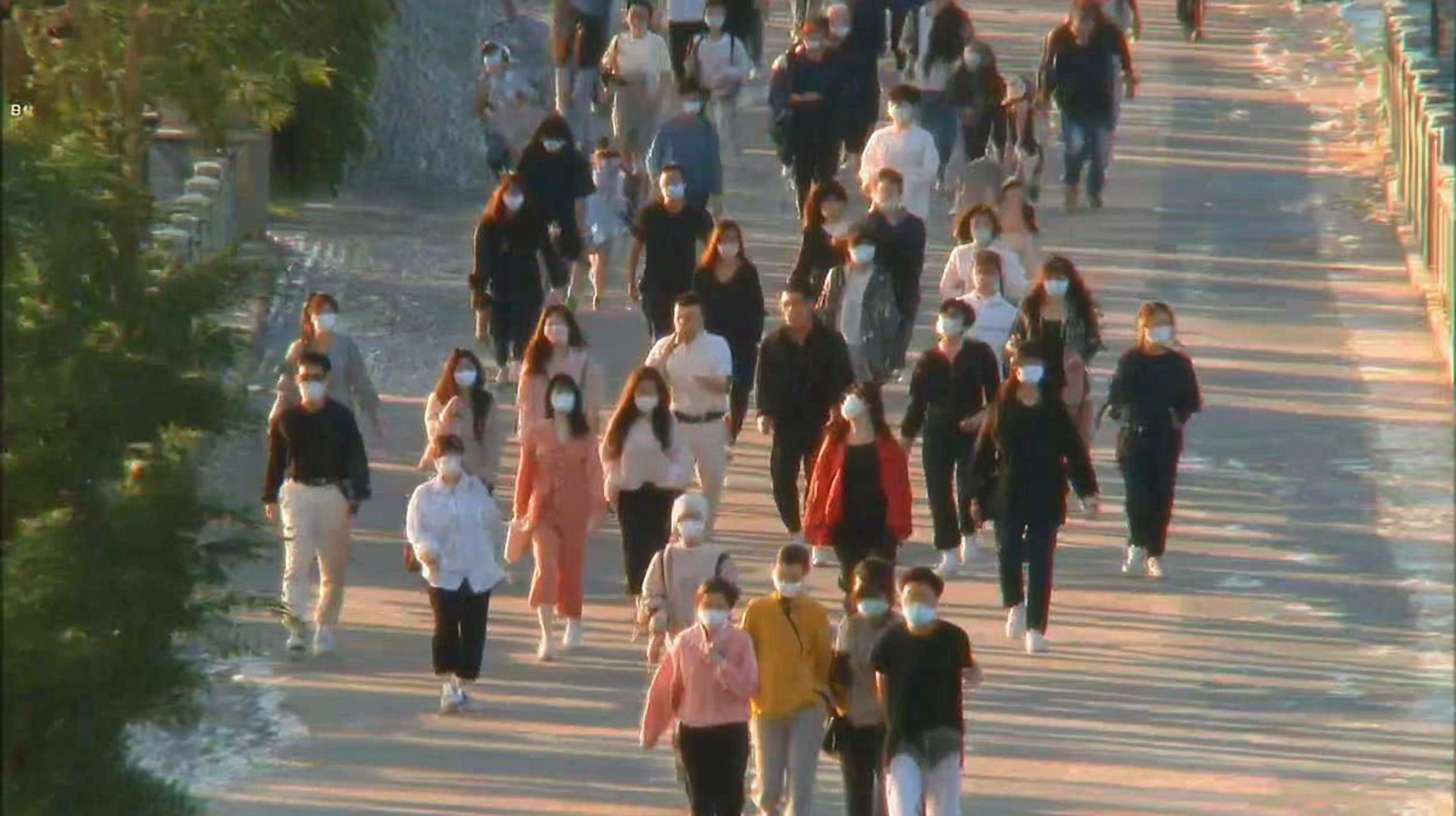 一群不同年龄段的人，包括亚洲人和白人，穿着各种颜色的衣服，如白色、粉色、黄色和黑色，大多数人戴着口罩，正在一个阳光明媚的日子里穿过一个宽敞的人行道。人行道上有明显的阴影，表明阳光从左侧照射。人们的姿势各异，有的正面朝向镜头，有的侧面或背面。画面风格为现实主义，整体氛围明亮而活跃。 --ar 16:9 --v 7 --stylize 100 --fast --sref https://img-xpc-mj0.xpccdn.com/prod/upload/a5ba7765-3f47-4272-9c97-a0abb955ceb6/%E6%88%AA%E5%B1%8F2025-08-01%2003.40.03.png~tplv-5yakomv5zn-auto-v1%3A1024%3A0%3Aq75.jpg --sw 310 --no 水印